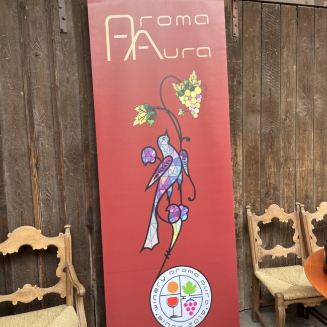Ein großes Plakat von Aroma Aura mit einem subtilen Bezug zu Arzach, der Heimat des Winzers, und Symbolen aus der armenischen Antike, darunter ein Vogel und Trauben.
